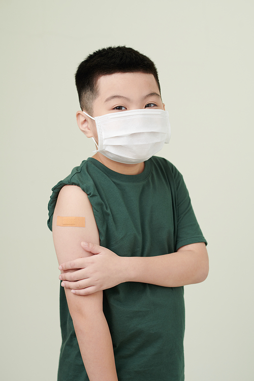 Portrait of little boy in medical mask with adhesive plaster over his covid-19 vaccine injection site