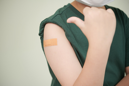 Cropped image of boy showing adhesive plaster he has on shoulder after vaccine injection