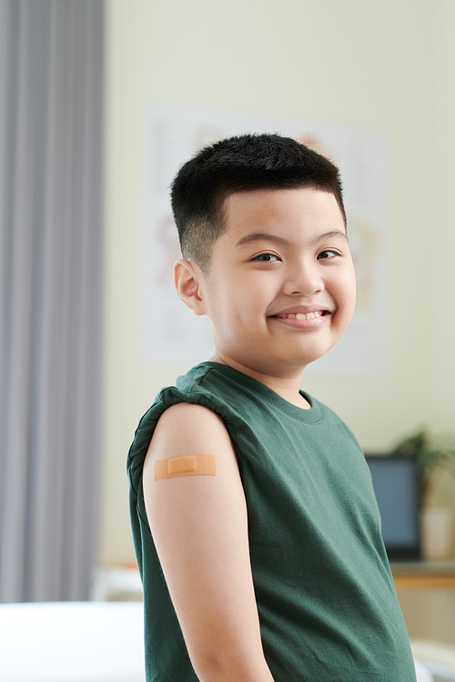 Portrait of smiling little boy with adhesive plaster on shoulder after accination against covid-19