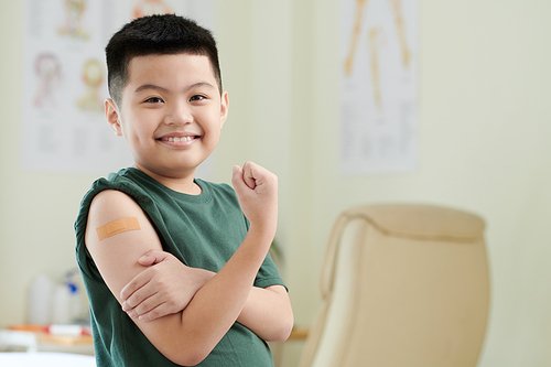 Cheerful boy happy to get injection of vaccine against coronavirus in shoulder