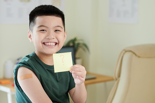 Smiling little boy vaccinated against coronavirus showing sticker with question mark