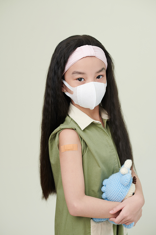 Preteen girl in medical mask standing with adhesive plaster on her shoulder