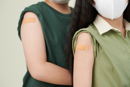 Close-up image of adhesive plasters on shoulders of vaccinated kids