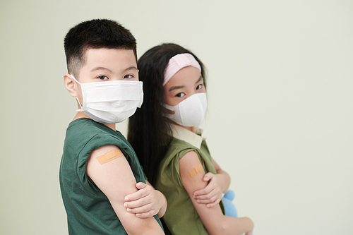 Kids in medical masks showing shoulder with adhesive plasters after they got vaccinated against coronavirus