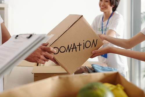Hands of man giving box with groceries and warm clothes to worker at donation center