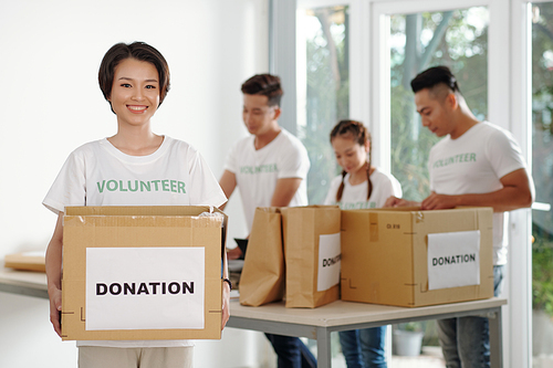 Portrait of happy young Vietnamese woman with big cardboard box working at donation center