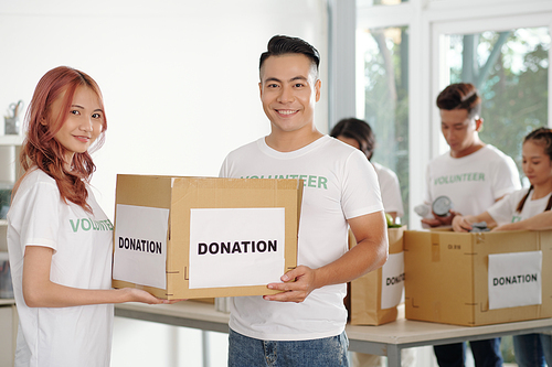 Young Asian couple working as volunteers in donation center, theay are packing boxed for people in need