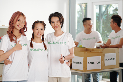 Portrait of hugging smiling young Asian woman showing thumbs-up when standing in donation center