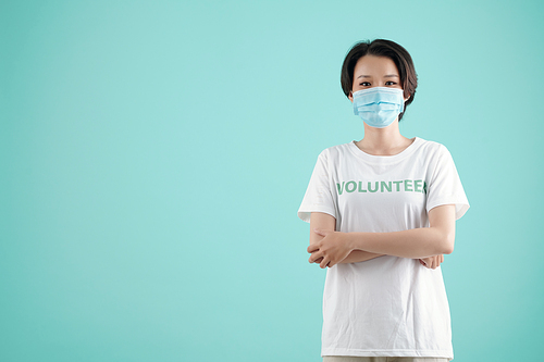 Pretty young Vietnamese volunteer in medical mask crossing arms and looking at camera