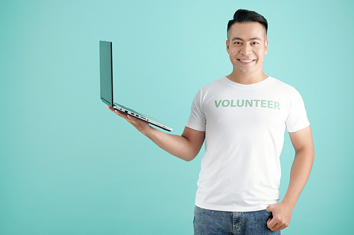 Portrait of happy young man with opened laptop in hand inviting you to sign up for volunteering work