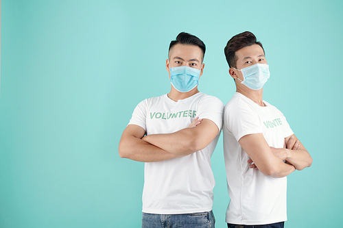 Portrait of confident handsome Asian volunteers in medical masks standing back to back and crossing arms