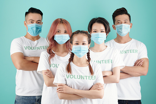 Team of young Vietnamese volunteers in protective masks standing behind their female leader