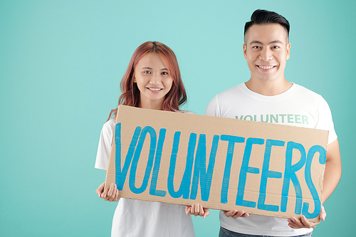 Smiling young Asian man and woman holding big sign with volunteers inscription