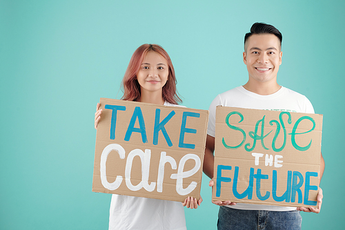 Young Asian activists holding two cardboard signs with take care and save the future inscriptions