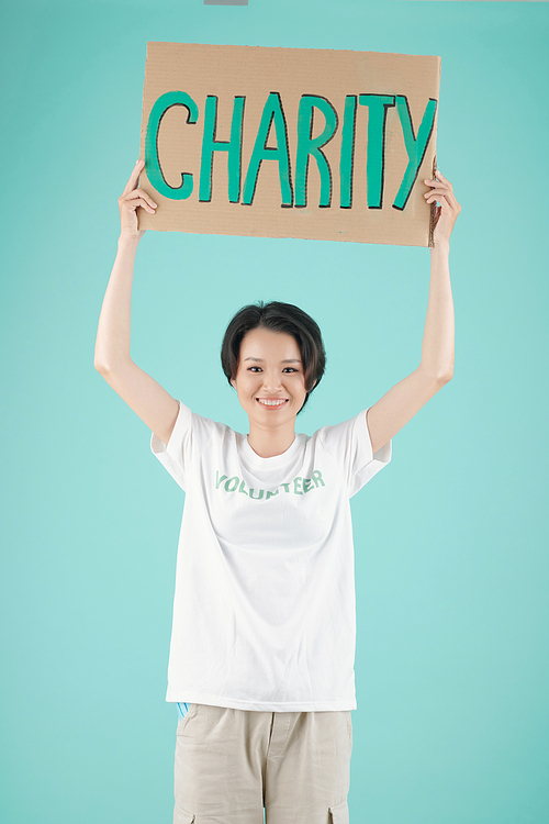 Smiling young Asian volunteer standing with charity placard, isolated on light blue