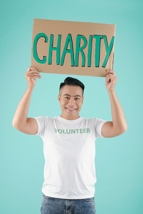 Portrait of handsome smiling young Asian man holding placard with charity inscription and looking at camera