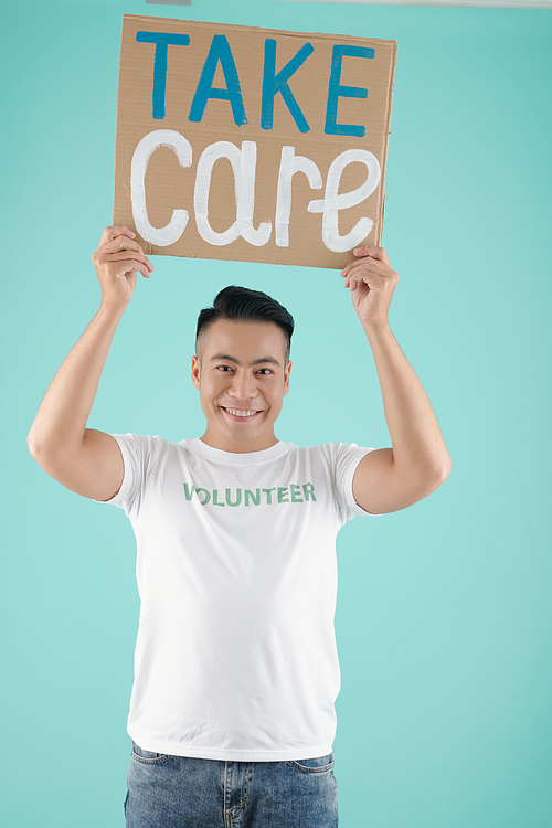 Positive volunteer of charity fund holding placard with take care inscription, isolated on turquoise