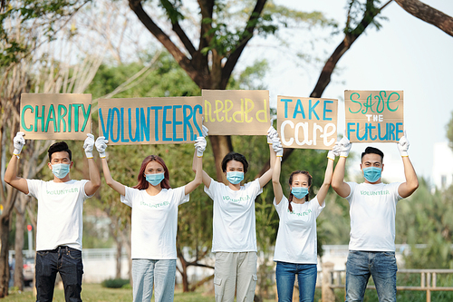 Team of young Asian volunteers raising placards over heads when promoting charity organization