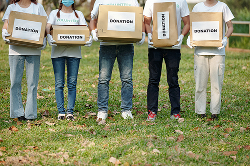 Cropped image of volunteers with donation boxes full of clothes and groceries standing park