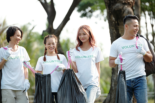 Cheerful students in volunteer t-shirts packing trash in park on college campus