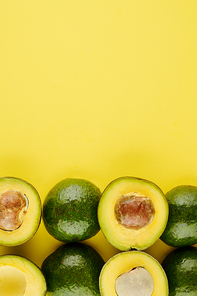 Yellow background with whole and cut avocados, healthy food and nutrition concept