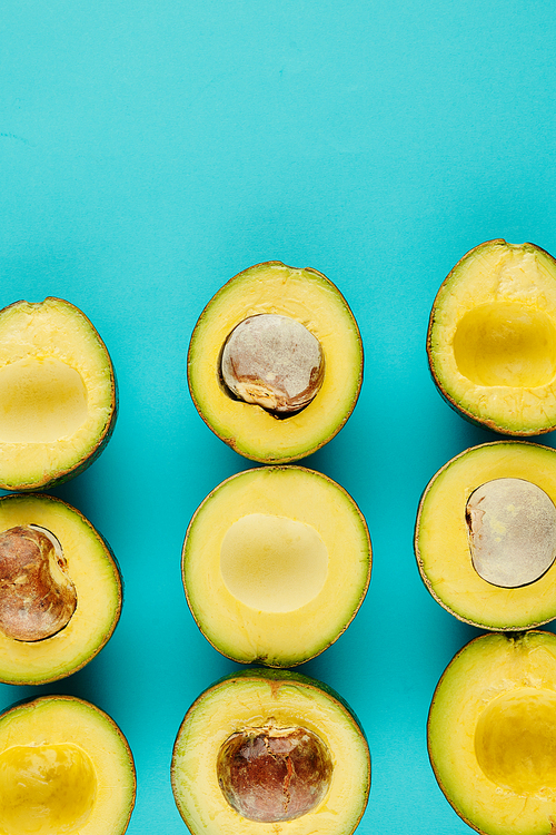 Delicous cut ripe avocados with and without cores on light blue background