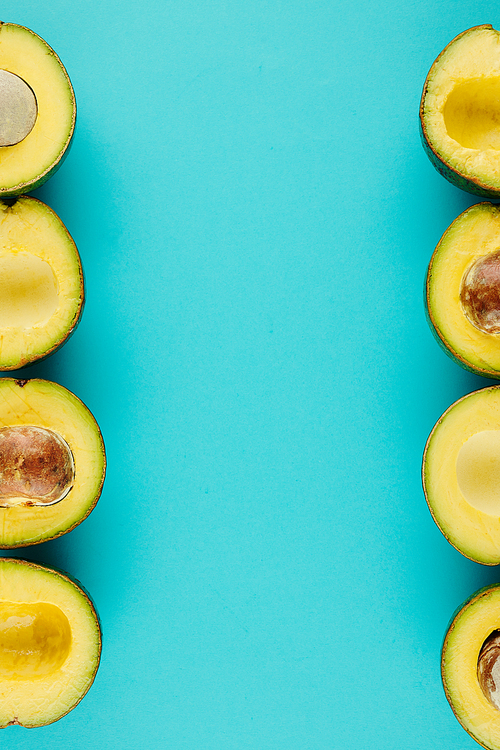 Fresh and ripe cut avocados on light blue surface, healthy snack background