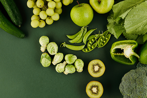 Green fruits and vegetables on table like kiwi, apples peas, grapes, pepper and brussels sprouts