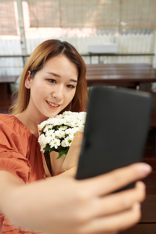 Smiling young woman taking selfie with bouquet of flowers