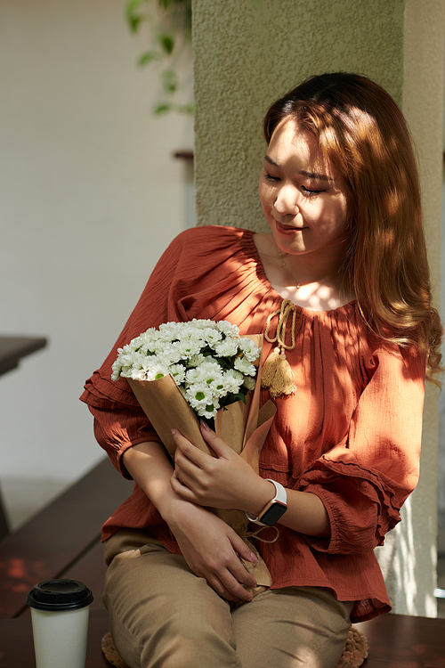 Smiling young woman looking at bouquet of fresh flowers in her hands