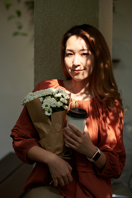 Portrait of positive young woman holding bouquet of beautiful flowers and smiling at camera