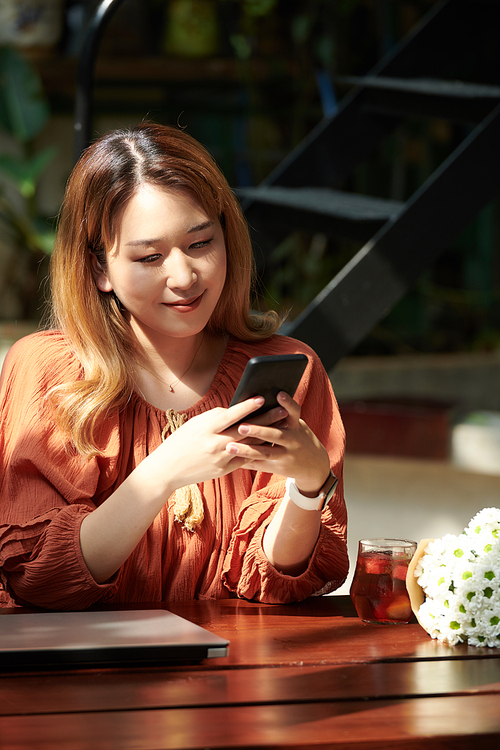 Smiling young woman reading text messages from her friend or boyfriend