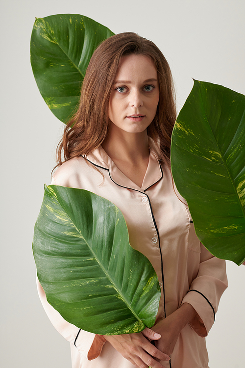 Young woman in silk pajamas standing among big green leaves