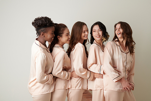 Group of cheerful female friends in silk pajamas standing one behind another