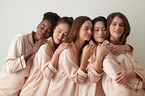 Sleepy young women in pajamas closing eyes and leaning on back of each other