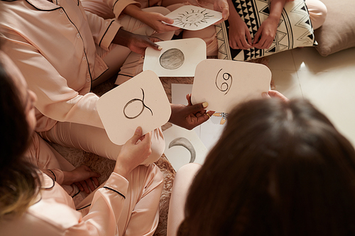 Hands of female friends discussing astrology and zodiac signs at sleepover party