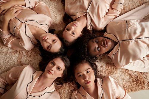 Diverse group of young women lying on the floor in circle head to head and looking up at camera