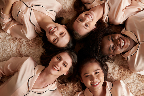 Multi-ethnic group of smiling young women in silk pajamas lying on the floor