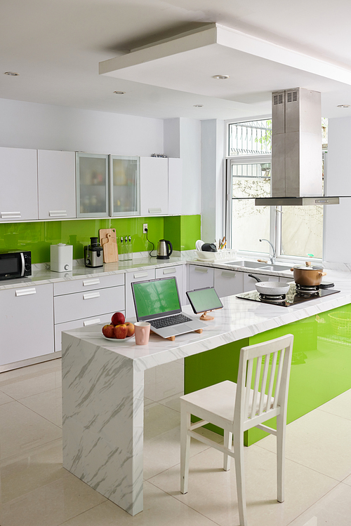 Interior of modern kitchen in spacious apartment with mobile gadgets with green screens on workplace of freelancer or home office worker