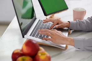 Side view of hands of young webdesigner pressing keys of laptop keypad while working over new mobile application or software