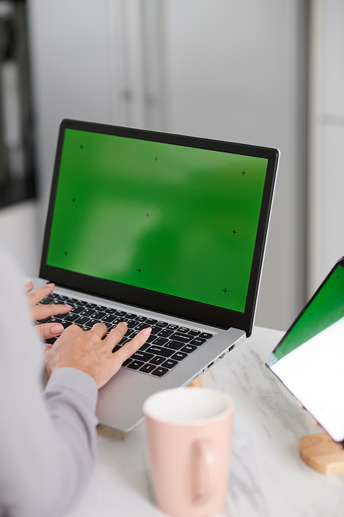 Hands of young female website designer working in front of green screen and pushing keys of laptop keypad while sitting by workplace