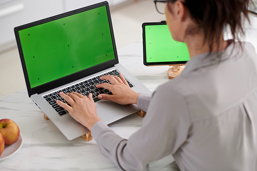 Close-up of young female programmer sitting in front of laptop with green screen and pressing buttons on keypad during work