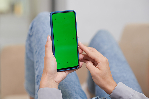 Hands of young modern woman holding mobile phone with blank green screen over ker legs in blue jeans and using new application