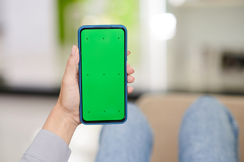Hand of young woman holding smartphone with black green screen while making advert or recommendation of new mobile application