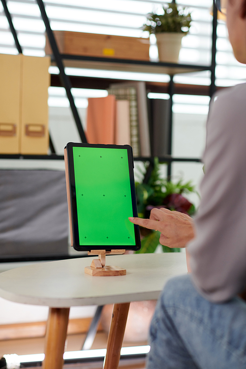 Close-up of young woman sitting in front of tablet and pointing at blank green screen while going to touch it and use new application