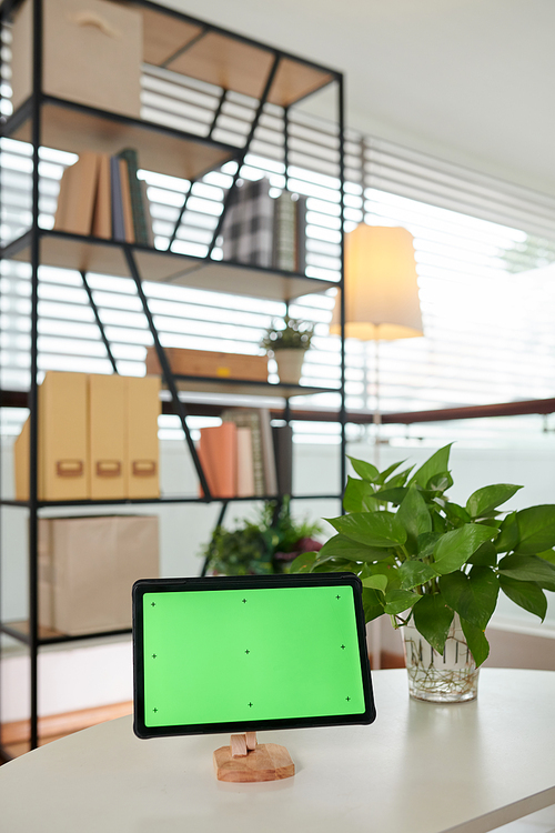 Workplace of modern home office worker with tablet with blank green screen on wooden holder standing on white table in living room