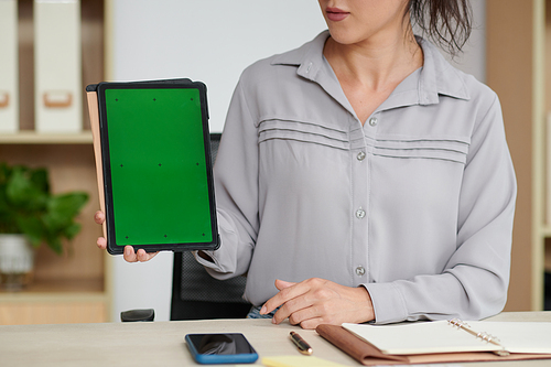 Cropped shot of young successful businesswoman making presentation while holding tablet with blank green screen by workplace