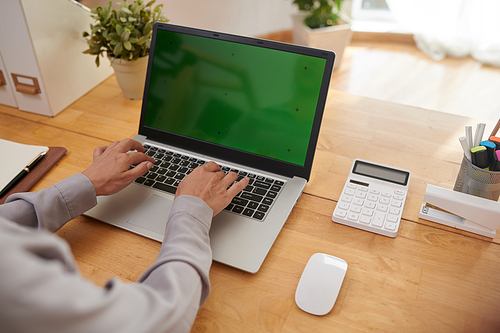 Hands of young modern female accountant over keypad with laptop with blank green screen using new mobile application during work