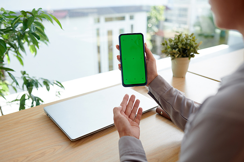 Hands of young female freelancer or software developer presenting new mobile application while holding smartphone with green screen