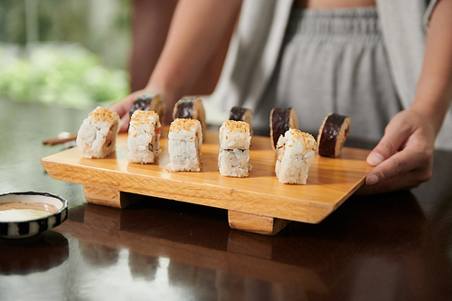 Woman putting wooden board with sushi on dinner table